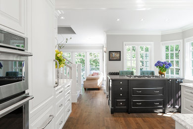 Large elegant l-shaped medium tone wood floor kitchen photo in Vancouver with an undermount sink, raised-panel cabinets, white cabinets, quartz countertops, white backsplash, ceramic backsplash, stainless steel appliances and an island