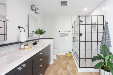 Example of a mid-sized trendy master white tile and subway tile vinyl floor, brown floor and double-sink corner shower design in Milwaukee with black cabinets, a two-piece toilet, an undermount sink, quartz countertops, a hinged shower door, white countertops, a niche, a built-in vanity, gray walls and shaker cabinets