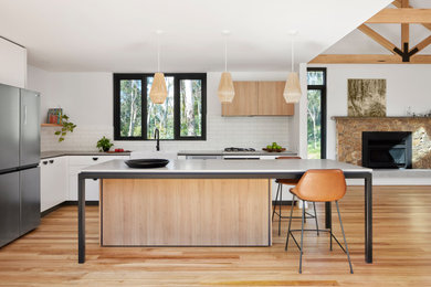 Inspiration for a contemporary l-shaped kitchen in Melbourne with a belfast sink, flat-panel cabinets, white cabinets, white splashback, metro tiled splashback, stainless steel appliances, light hardwood flooring, an island, beige floors and grey worktops.