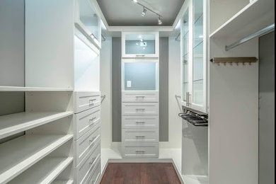 Diseño de armario vestidor unisex moderno de tamaño medio con armarios con paneles lisos, puertas de armario blancas, suelo de madera oscura y suelo marrón