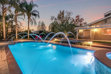 Photo of a mid-sized transitional backyard custom-shaped pool in Orange County with a hot tub and brick pavers.