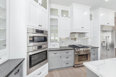 This is an example of a mid-sized contemporary l-shaped eat-in kitchen in Sacramento with a single-bowl sink, flat-panel cabinets, white cabinets, marble benchtops, grey splashback, marble splashback, stainless steel appliances, light hardwood floors, with island, beige floor and black benchtop.