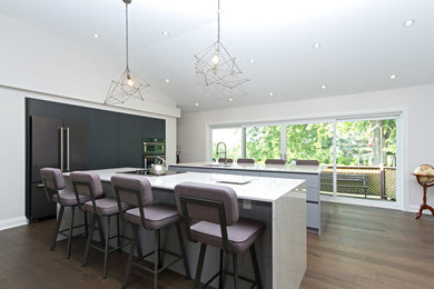 This is an example of a large modern kitchen in Toronto with an undermount sink, flat-panel cabinets, black cabinets, quartz benchtops, panelled appliances, medium hardwood floors, multiple islands and brown floor.