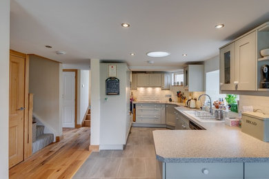 Design ideas for a medium sized classic l-shaped open plan kitchen in Cornwall with a double-bowl sink, recessed-panel cabinets, white cabinets, composite countertops, white splashback, ceramic splashback, white appliances, vinyl flooring and grey floors.