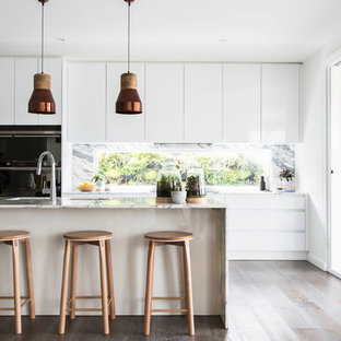 Inspiration pour une arrière-cuisine parallèle nordique avec un placard à porte plane, des portes de placard blanches, une crédence en fenêtre, un sol en bois foncé, un îlot central, un sol marron, un plan de travail en marbre, un électroménager noir et un plan de travail blanc.