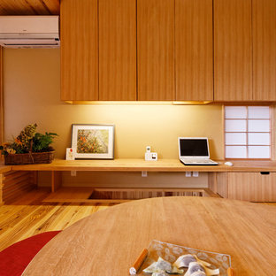 This is an example of a small modern home office and library in Other with beige walls, medium hardwood flooring, a wood burning stove, a stone fireplace surround, a built-in desk and brown floors.