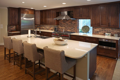 Example of a large arts and crafts l-shaped light wood floor open concept kitchen design in Charlotte with a farmhouse sink, flat-panel cabinets, dark wood cabinets, quartz countertops, brown backsplash, stainless steel appliances, an island and brick backsplash