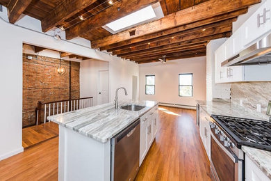 Example of a mid-sized urban galley medium tone wood floor open concept kitchen design in Phoenix with an undermount sink, shaker cabinets, white cabinets, quartzite countertops, gray backsplash, stone slab backsplash, stainless steel appliances and an island