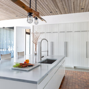 Photo of a mid-sized country u-shaped eat-in kitchen in Los Angeles with an undermount sink, louvered cabinets, white cabinets, solid surface benchtops, stainless steel appliances, terra-cotta floors, with island, orange floor, white benchtop and wood.