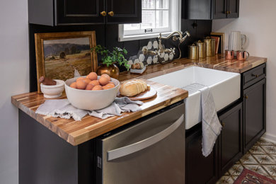 Mid-sized transitional u-shaped ceramic tile and multicolored floor enclosed kitchen photo in Indianapolis with a farmhouse sink, shaker cabinets, black cabinets, wood countertops, black backsplash, shiplap backsplash, stainless steel appliances, no island and brown countertops