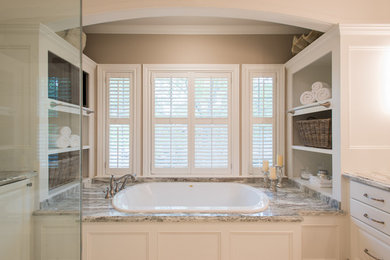 This is an example of a large transitional master bathroom in Houston with raised-panel cabinets, white cabinets, a drop-in tub, a one-piece toilet, beige tile, porcelain tile, white walls, limestone floors, an undermount sink, engineered quartz benchtops and a corner shower.