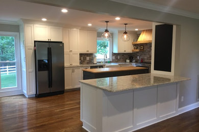 Photo of a mid-sized transitional u-shaped open plan kitchen in Charlotte with a farmhouse sink, shaker cabinets, white cabinets, granite benchtops, grey splashback, brick splashback, stainless steel appliances, medium hardwood floors, with island and brown floor.