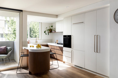 Design ideas for a contemporary u-shaped eat-in kitchen in Melbourne with an undermount sink, flat-panel cabinets, white cabinets, quartz benchtops, white splashback, white appliances, medium hardwood floors, a peninsula, brown floor and white benchtop.