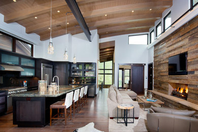 Large mountain style open concept dark wood floor living room photo in Denver with brown walls, a standard fireplace, a stone fireplace and a wall-mounted tv