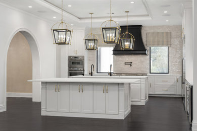 Kitchen - huge transitional l-shaped dark wood floor and black floor kitchen idea in Houston with an undermount sink, shaker cabinets, white cabinets, white backsplash, terra-cotta backsplash, white appliances, two islands and white countertops