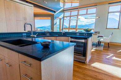 Eat-in kitchen - mid-sized modern u-shaped light wood floor and brown floor eat-in kitchen idea in Denver with flat-panel cabinets, light wood cabinets, limestone countertops, blue backsplash, glass tile backsplash, stainless steel appliances and an island