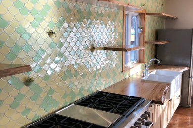 Eclectic medium tone wood floor and brown floor kitchen photo in Minneapolis with a farmhouse sink, yellow cabinets, wood countertops, multicolored backsplash, mosaic tile backsplash, stainless steel appliances, an island and brown countertops