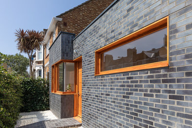 This is an example of a mid-sized contemporary front door in London with grey walls, brick floors, a single front door, a medium wood front door and grey floor.