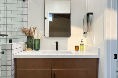 Example of a mid-sized transitional master white tile and ceramic tile porcelain tile, black floor and single-sink bathroom design in San Diego with flat-panel cabinets, brown cabinets, a one-piece toilet, white walls, an undermount sink, quartz countertops, a hinged shower door, white countertops and a built-in vanity