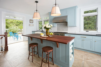 Large transitional eat-in kitchen in New York with a farmhouse sink, beaded inset cabinets, blue cabinets, wood benchtops, multi-coloured splashback, ceramic splashback, stainless steel appliances, porcelain floors, with island, beige floor and brown benchtop.