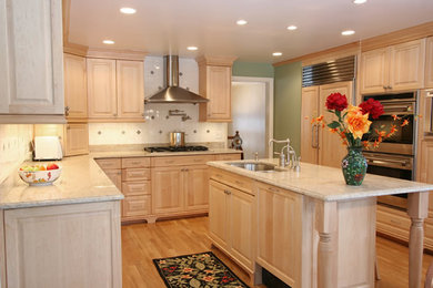 Inspiration for a mid-sized timeless u-shaped medium tone wood floor and brown floor kitchen remodel in Boston with an undermount sink, raised-panel cabinets, light wood cabinets, granite countertops, white backsplash, ceramic backsplash, stainless steel appliances and an island