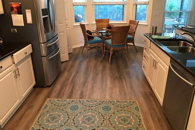 Photo of a mid-sized beach style galley eat-in kitchen in Jacksonville with an undermount sink, recessed-panel cabinets, white cabinets, granite benchtops, stainless steel appliances, laminate floors, no island and brown floor.