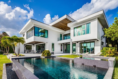 This is an example of a large contemporary two-storey stucco white house exterior in Miami with a flat roof.