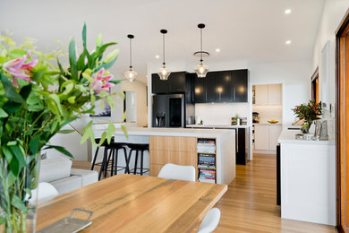 Large contemporary u-shaped open plan kitchen in Brisbane with an undermount sink, recessed-panel cabinets, white cabinets, quartz benchtops, white splashback, subway tile splashback, black appliances, light hardwood floors, with island, brown floor and white benchtop.