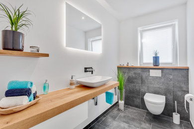 Modernes Badezimmer mit hellen Holzschränken, schwarz-weißen Fliesen, Aufsatzwaschbecken, Waschtisch aus Holz, Einzelwaschbecken und schwebendem Waschtisch in Sonstige