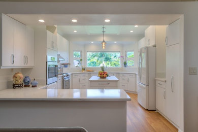 Design ideas for a large transitional u-shaped separate kitchen in Hawaii with an undermount sink, flat-panel cabinets, white cabinets, quartz benchtops, white appliances, medium hardwood floors, with island and brown floor.