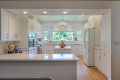 Example of a large transitional u-shaped medium tone wood floor and brown floor enclosed kitchen design in Hawaii with an undermount sink, flat-panel cabinets, white cabinets, quartz countertops, white appliances and an island
