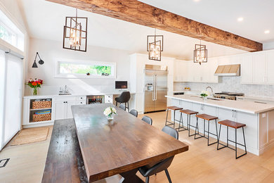 Large transitional l-shaped light wood floor and beige floor kitchen photo in Toronto with a double-bowl sink, shaker cabinets, white cabinets, wood countertops, white backsplash, mosaic tile backsplash, stainless steel appliances, an island and white countertops