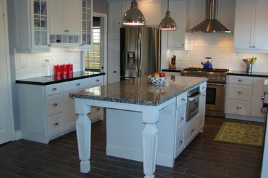 Example of a mid-sized transitional u-shaped porcelain tile eat-in kitchen design in Orange County with a farmhouse sink, shaker cabinets, white cabinets, granite countertops, white backsplash, subway tile backsplash, stainless steel appliances and an island