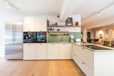Foto de cocinas en L tradicional de tamaño medio abierta con electrodomésticos negros, suelo de madera en tonos medios y península