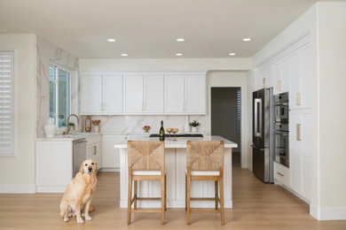 Inspiration for a transitional u-shaped vinyl floor and brown floor eat-in kitchen remodel in Orange County with an undermount sink, shaker cabinets, white cabinets, quartz countertops, white backsplash, quartz backsplash, stainless steel appliances, an island and white countertops