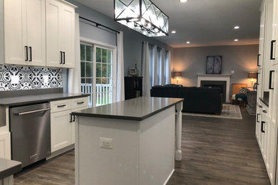 Mid-sized farmhouse l-shaped vinyl floor and gray floor eat-in kitchen photo in DC Metro with a farmhouse sink, shaker cabinets, white cabinets, quartz countertops, black backsplash, porcelain backsplash, stainless steel appliances, an island and gray countertops