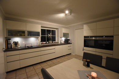 Zweizeilige, Große Moderne Wohnküche ohne Insel mit Waschbecken, flächenbündigen Schrankfronten, weißen Schränken, Arbeitsplatte aus Holz, Küchenrückwand in Weiß, Glasrückwand, schwarzen Elektrogeräten und brauner Arbeitsplatte in Sonstige