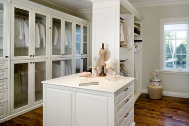This is an example of a large traditional gender neutral walk-in wardrobe in New York with glass-front cabinets, white cabinets and medium hardwood flooring.