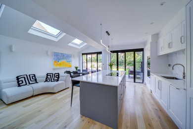 Photo of a contemporary grey and white kitchen in London with recessed-panel cabinets, quartz worktops, white splashback, engineered quartz splashback, painted wood flooring, an island, brown floors, white worktops and a vaulted ceiling.
