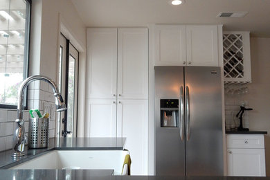 Inspiration for a mid-sized transitional terra-cotta tile and brown floor kitchen remodel in Orange County with a farmhouse sink, shaker cabinets, white cabinets, solid surface countertops, white backsplash, subway tile backsplash, stainless steel appliances, a peninsula and black countertops