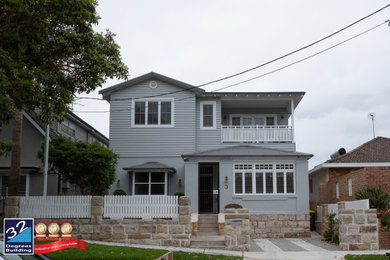 Large beach style two-storey grey house exterior in Sydney with wood siding, a gable roof and a metal roof.