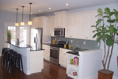 Large trendy single-wall medium tone wood floor kitchen photo in Philadelphia with an island, recessed-panel cabinets, an undermount sink, white cabinets, multicolored backsplash, glass tile backsplash and stainless steel appliances