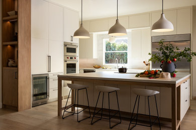 Example of a large trendy l-shaped medium tone wood floor, brown floor and vaulted ceiling kitchen pantry design in Sacramento with an undermount sink, flat-panel cabinets, white cabinets, solid surface countertops, white backsplash, porcelain backsplash, stainless steel appliances, an island and white countertops