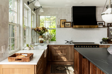 Eat-in kitchen - large transitional u-shaped light wood floor and brown floor eat-in kitchen idea in Detroit with a farmhouse sink, shaker cabinets, light wood cabinets, soapstone countertops, white backsplash, terra-cotta backsplash, black appliances, an island and black countertops