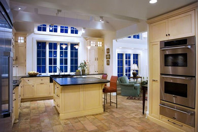 Inspiration for a mid-sized timeless l-shaped terra-cotta tile and multicolored floor enclosed kitchen remodel in Newark with a farmhouse sink, beaded inset cabinets, beige cabinets, beige backsplash, stone tile backsplash, stainless steel appliances, an island and soapstone countertops
