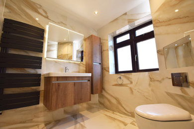 Medium sized modern cream and black ensuite bathroom in London with medium wood cabinets, a walk-in shower, a wall mounted toilet, beige tiles, beige walls, a built-in sink, solid surface worktops, an open shower, white worktops, a feature wall, a single sink and a floating vanity unit.