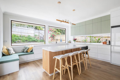 This is an example of a mid-sized contemporary l-shaped open plan kitchen in Sydney with a double-bowl sink, open cabinets, green cabinets, quartz benchtops, white splashback, glass sheet splashback, black appliances, medium hardwood floors, with island, multi-coloured floor and white benchtop.