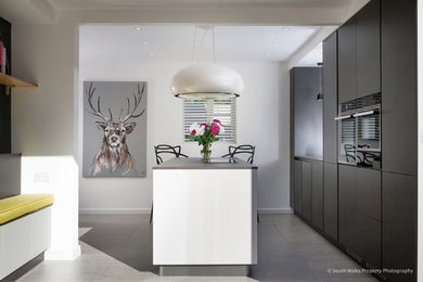 Photo of a small contemporary single-wall kitchen/diner in Other with flat-panel cabinets, black cabinets, composite countertops, black appliances, ceramic flooring, an island, grey floors and black worktops.