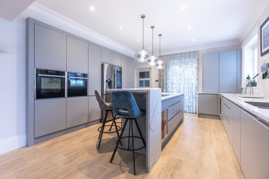 Inspiration for a medium sized modern l-shaped open plan kitchen in Other with a submerged sink, flat-panel cabinets, grey cabinets, quartz worktops, white splashback, stone slab splashback, integrated appliances, light hardwood flooring, an island, beige floors and white worktops.