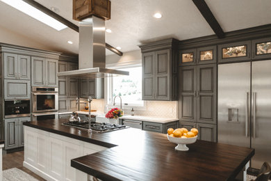 Mid-sized farmhouse l-shaped dark wood floor and brown floor eat-in kitchen photo in Other with a farmhouse sink, raised-panel cabinets, gray cabinets, quartz countertops, white backsplash, ceramic backsplash, stainless steel appliances, an island and white countertops